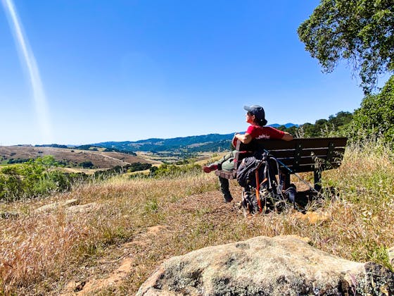 Hiker on a bench overlooking the vast scenery of mountains at Santa Teresa County Park in San Jose 