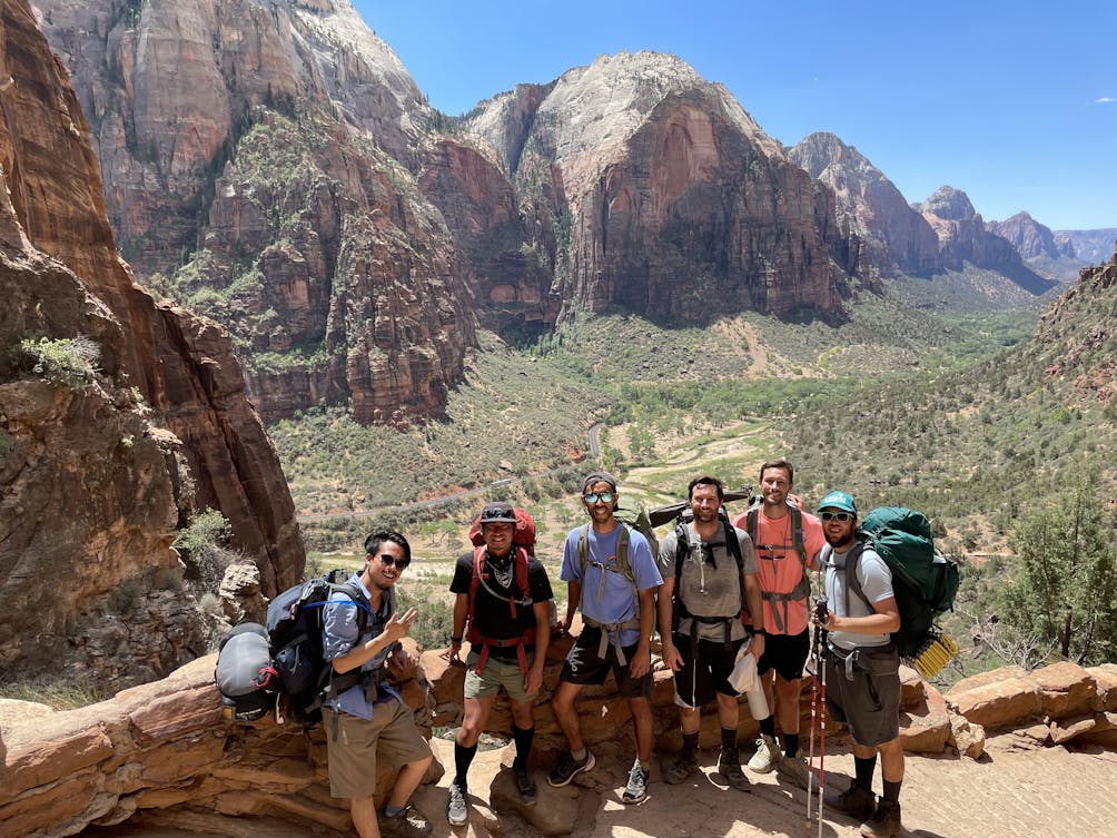 Group of friends backpacking and posing for a photo in front o granite mountains in Zion National Park 