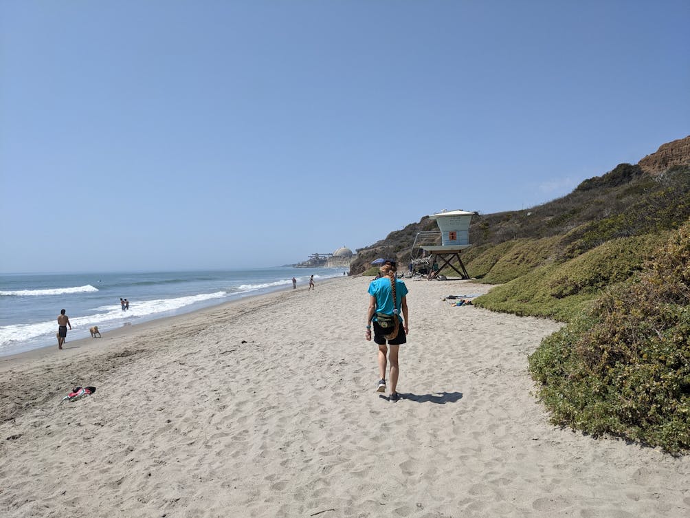 Woman walking along the sand towards a lifeguard tower on San Onofre State Beach in San Diego County 