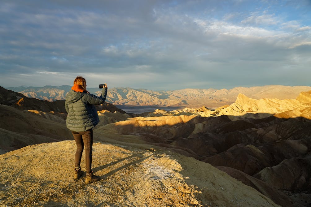 A woman taking a photo of sunrise from Zabriskie Point in Death Valley National Park 