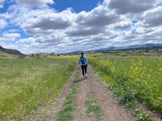 A woman on a hiking trail with huge open space and yellow flowers around her at Wildwood Park in Thousand Oaks