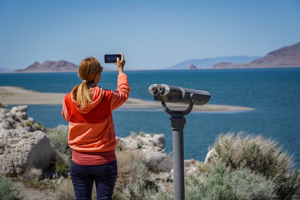 A woman takes a photo of Pyramid Lake with her phone 