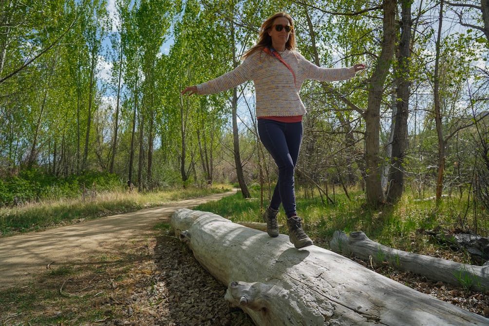 A woman walks along a fallen tree log at Oxbow Nature Study Area 