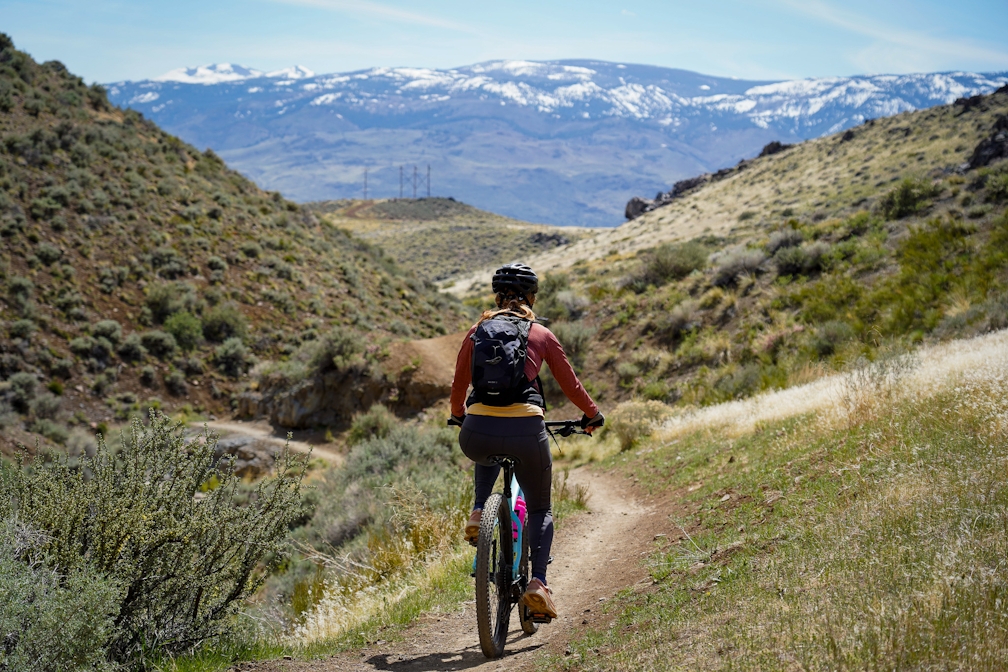A woman mountain biking at Keystone Canyon in Reno; snowcapped mountains are in the background