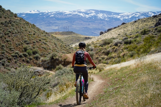 A woman mountain biking at Keystone Canyon in Reno; snowcapped mountains are in the background