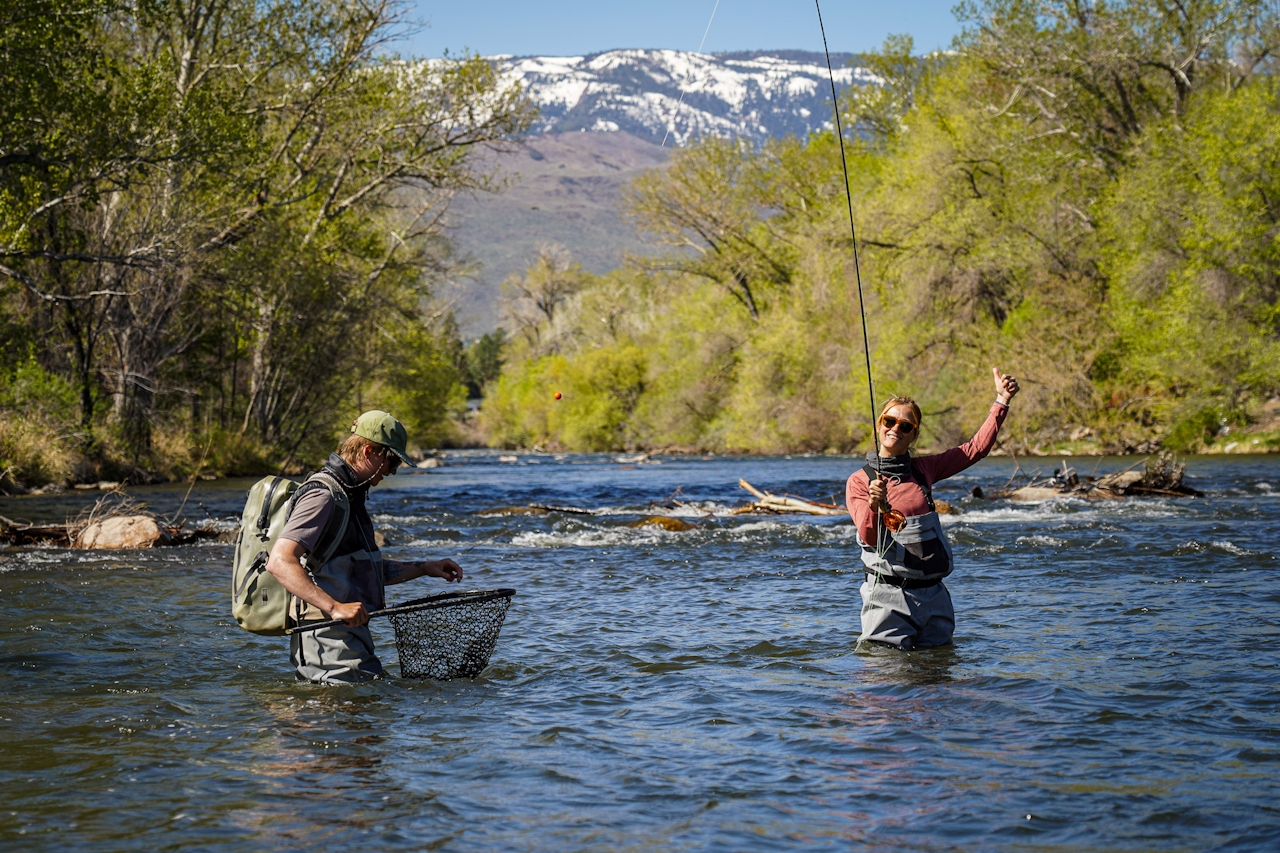 Two people in the Truckee River wearing waders with a snow capped mountain in the background on a Reno Fly Shop guided adveture
