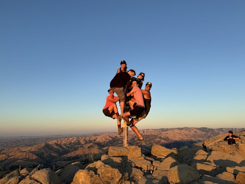A group of people clamored around the summit marker at Mission Peak in the Bay Area 