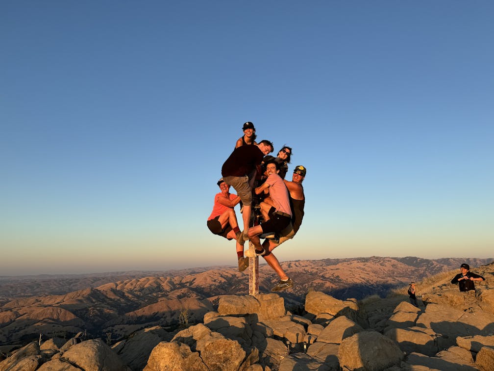 A group of people clamored around the summit marker at Mission Peak in the Bay Area 