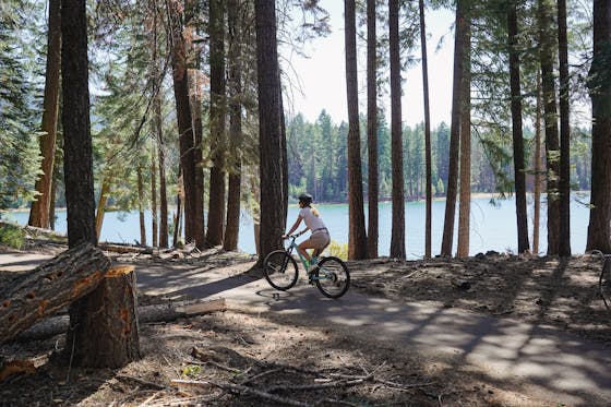 A woman is riding her bike past trees and Lake Almanor in Chester 