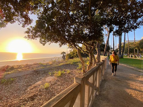 A woman walks the path next to the beach at sunset at Palisades Park in Los Angeles County