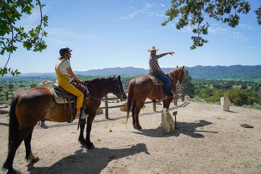 A woman on a horse looks out to the mountainous scenery that a man on another horse is pointing towards in Paso Robles at the historic Santa Margarita Ranch with Central Coast Trail Rides