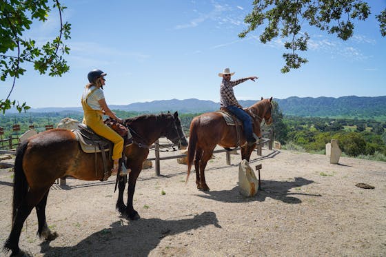 A woman on a horse looks out to the mountainous scenery that a man on another horse is pointing towards in Paso Robles at the historic Santa Margarita Ranch with Central Coast Trail Rides