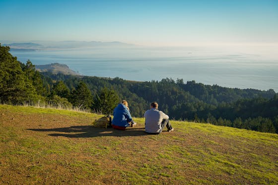Two people sit and look out to the ocean at Mount Tam