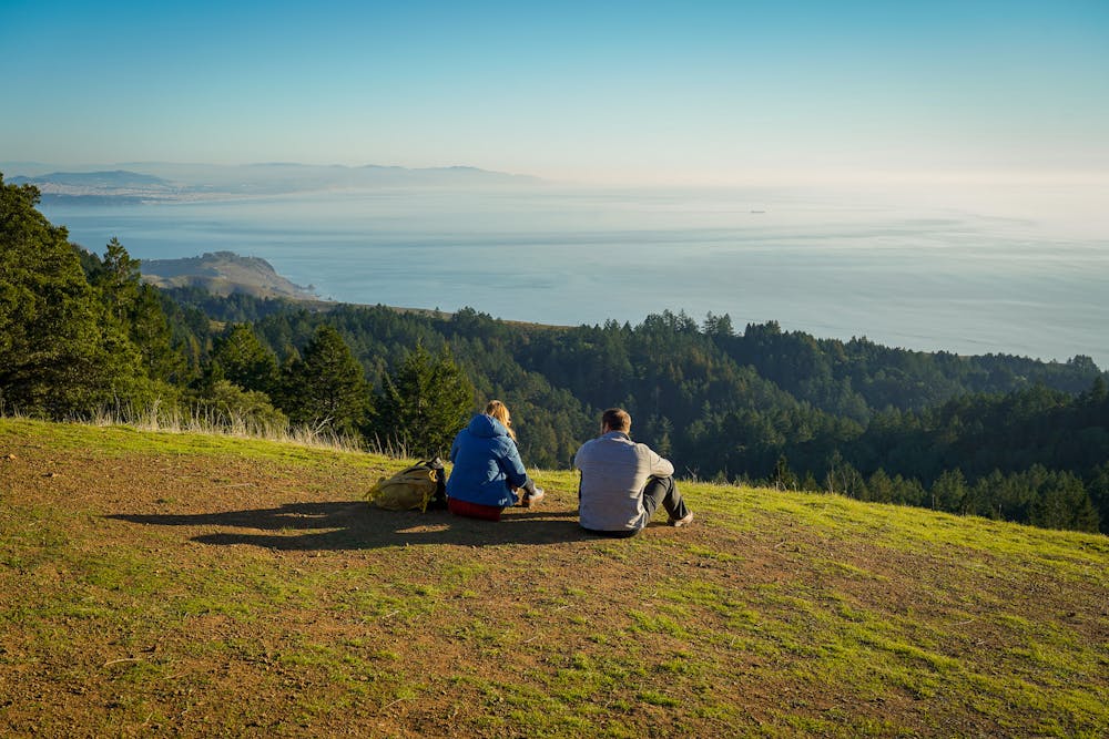 Two people sit and look out to the ocean at Mount Tam
