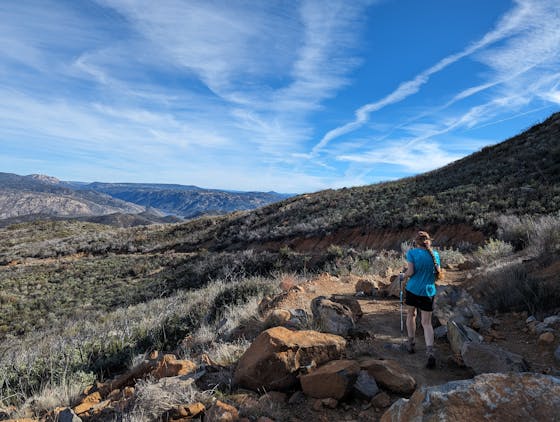 A woman hiker in a light blue shirt points out at the mountains on a hike called Lawson Peak in Southern California