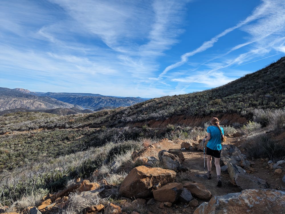 A woman hiker in a light blue shirt points out at the mountains on a hike called Lawson Peak in Southern California