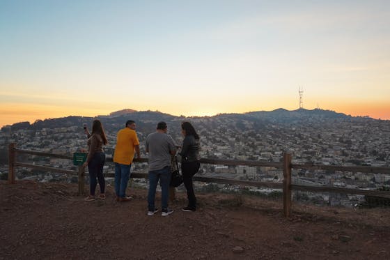 A group of friends hangs out at the top of Bernal Heights Park in San Francisco, looking out at the sunset