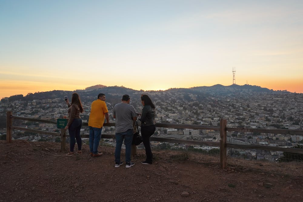 A group of friends hangs out at the top of Bernal Heights Park in San Francisco, looking out at the sunset