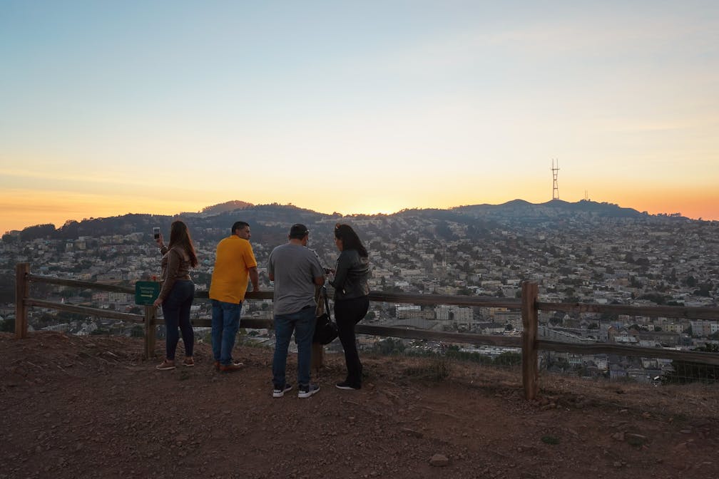 A group of friends hangs out at the top of Bernal Heights Park in San Francisco, looking out at the sunset