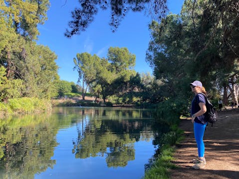 A woman standing at the pond's edge at Ernest B Debs Regional Park in Los Angeles. Trees are making reflections on the pond.