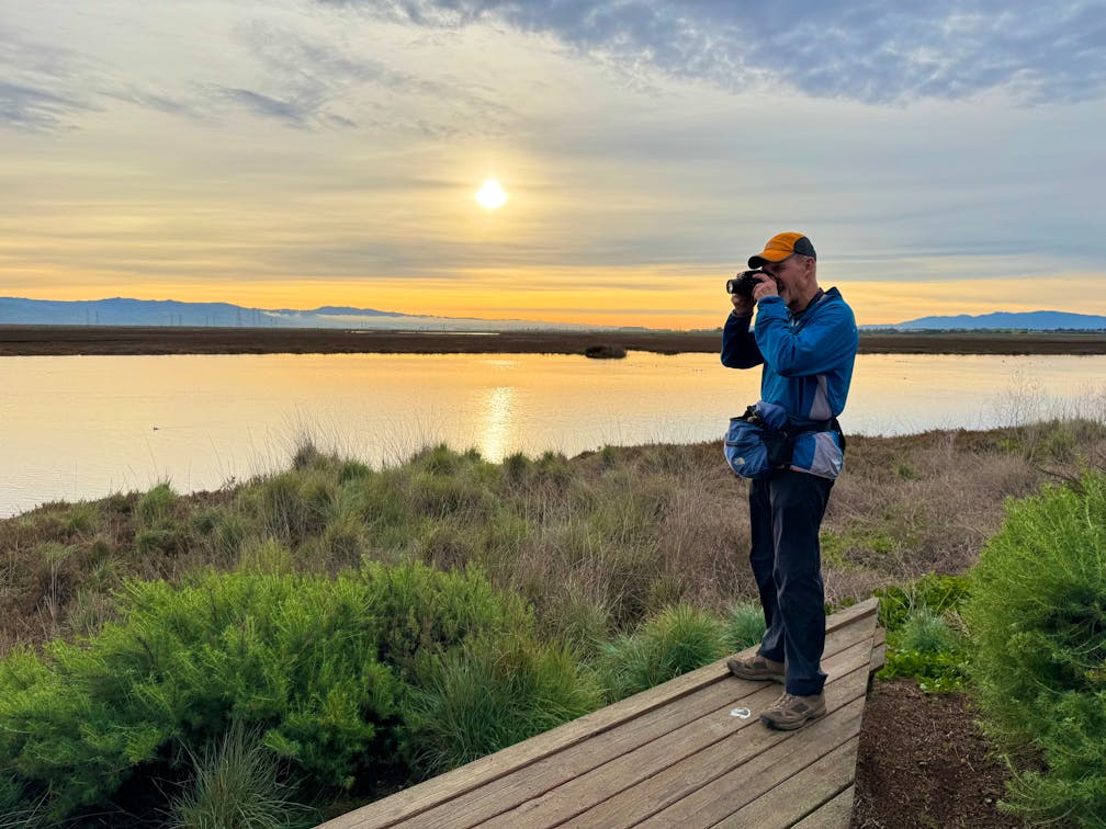 A man is looking through his binoculars at sunrise at the Bayland Nature Preserve in Palo Alto