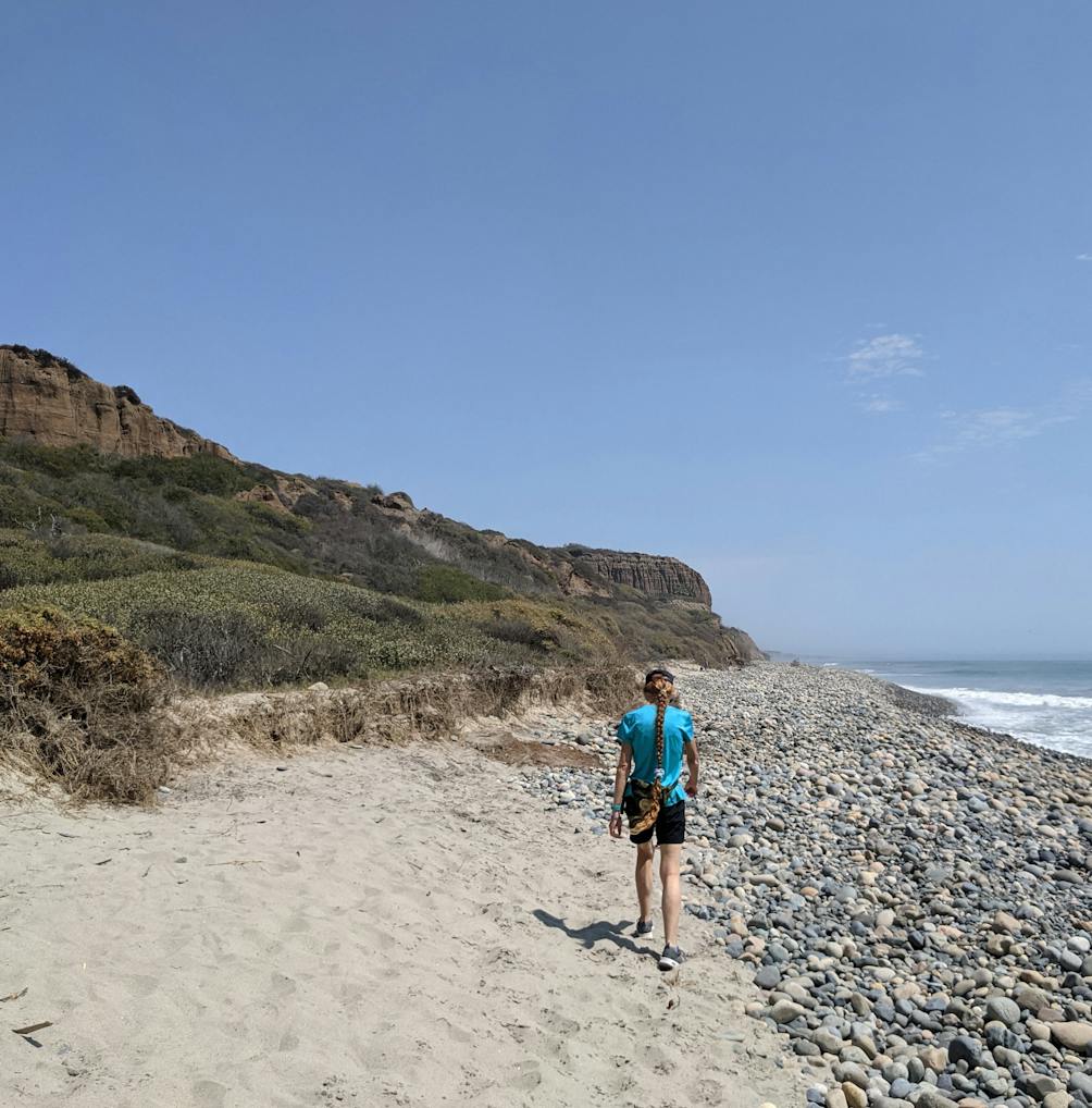 Woman walking on the sandy beach next to a rocky section on San Onofre State Beach in San Diego County 