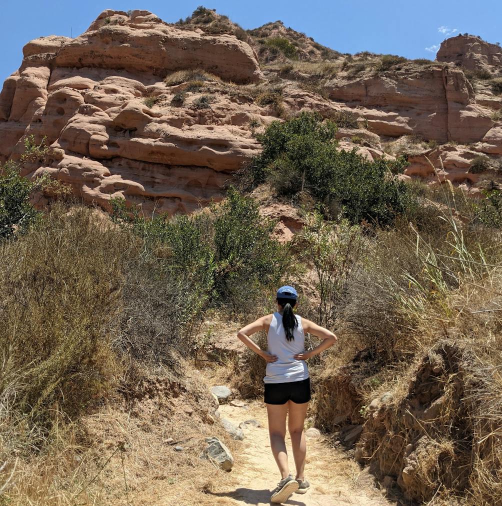 Woman standing on a hiking trail staring at giant red rock formation in front of her at Whiting Ranch Wilderness Park in Orange County 