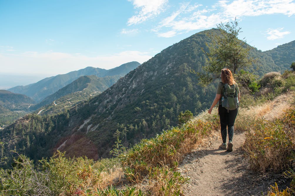 Woman hiking on the Bear Canyon Trail in Angeles National Forest and surrounded by huge mountain views on Mount Baldy in Los Angeles County