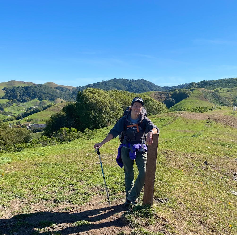 Hiker standing at a trail sign with green rolling hills and trees in the background at Carr Ranch in Contra Costa County 