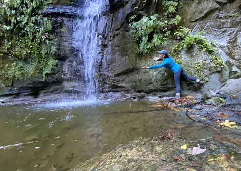 Woman hiking reaching out towards Maple Falls in The Forest of Nisene Marks State Park