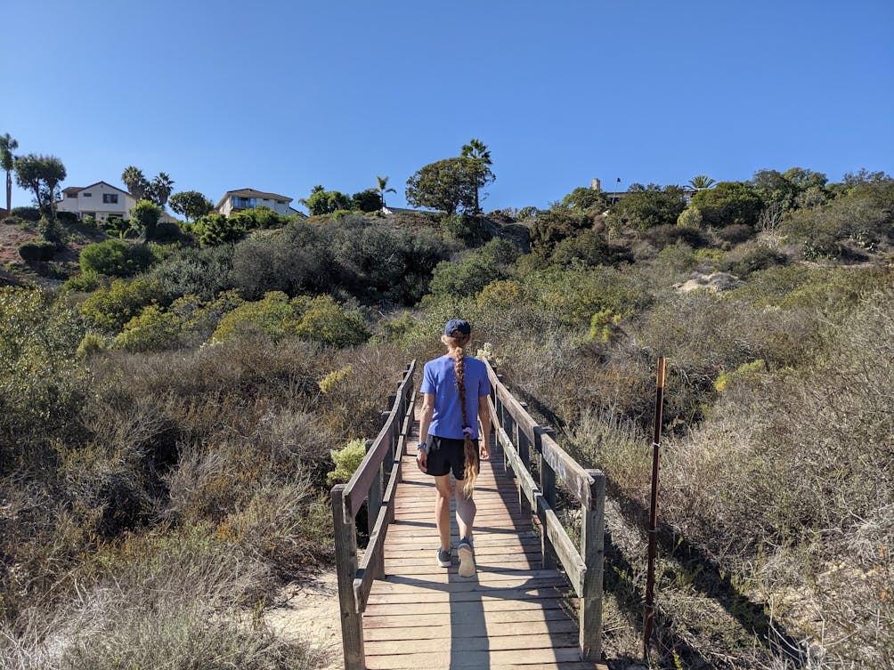 A hiker crosses a bridge amid chaparral scenery at Manchester Preserve in North San Diego County 