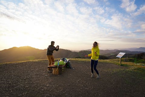 Two hikers laughing and taking photos at the sunset at the summit of Bald Mountain in Sugarloaf Ridge State Park