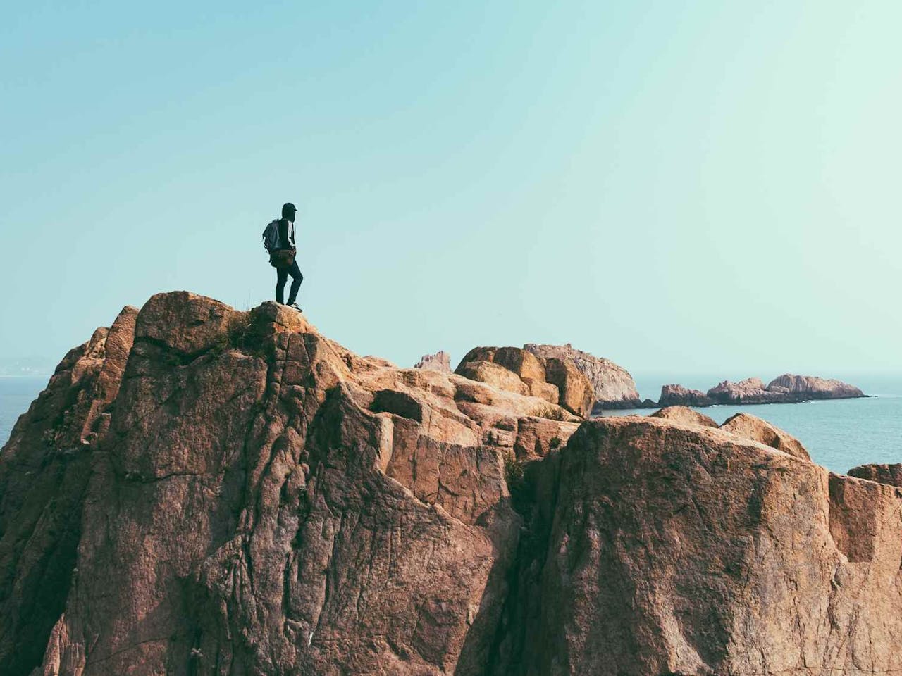 Person standing on top of rock crop, overlooking the sea