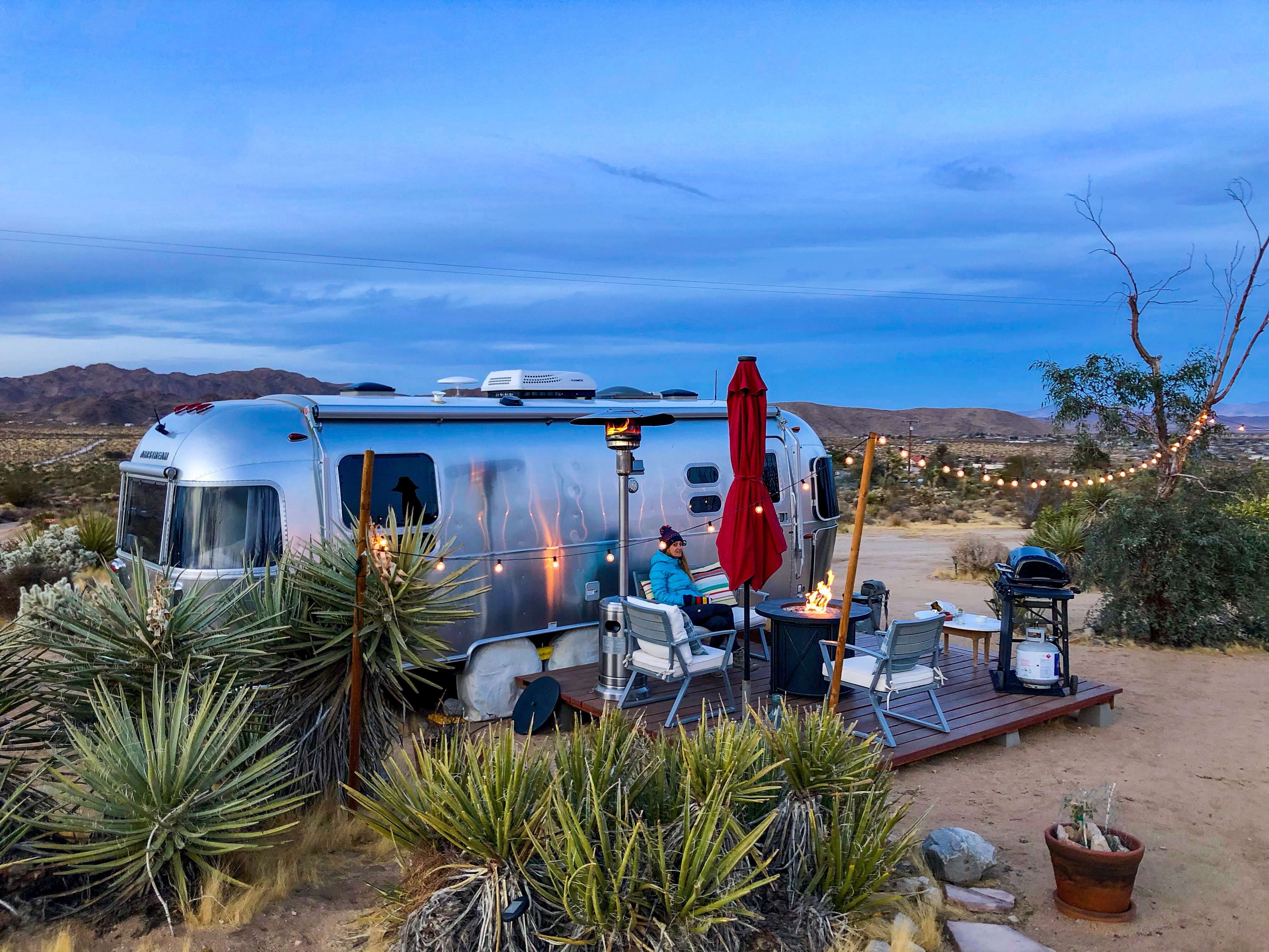 Person sitting by a firepit near a trailer in the desert