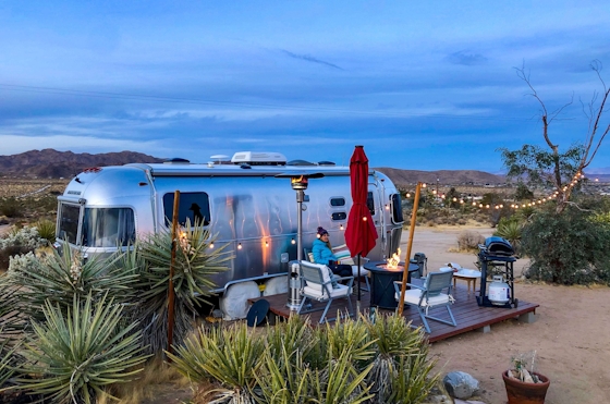 Person sitting by a firepit near a trailer in the desert