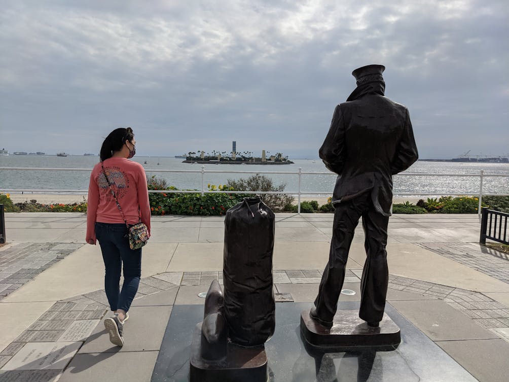 Woman standing with The Lone Sailor sculpture in Long Beach 