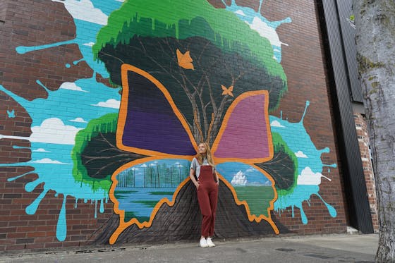 woman standing at a colorful butterfly mural amid the mural art project in Roseburg