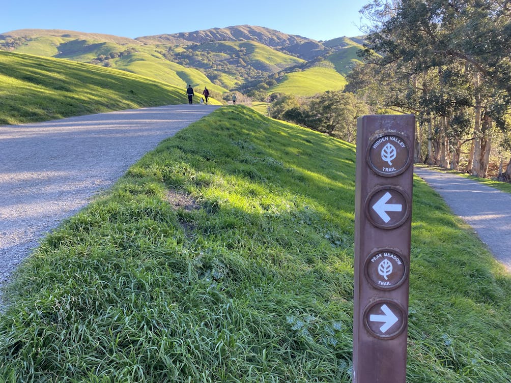 Signage and a hiking trail with hikers heading toward the hills and Mission Peak in the East Bay 