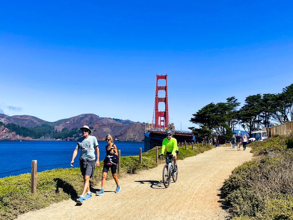 Bikers and walkers on the Bay Area Ridge Trail with the Golden Gate Bridge behind them 
