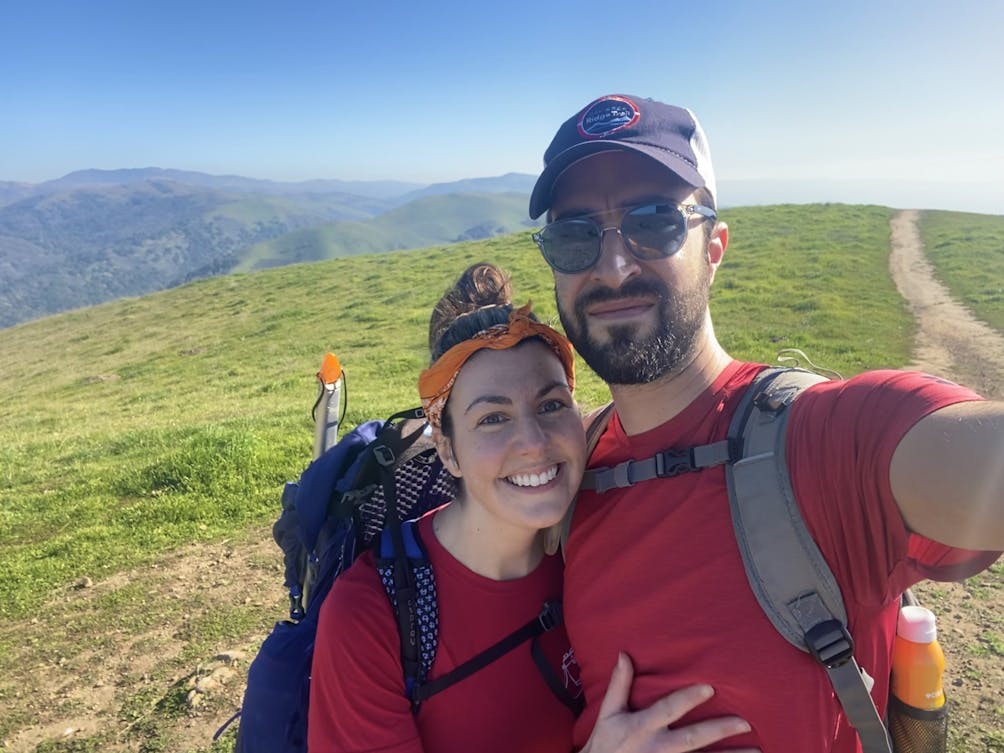 Couple taking a selfie picture at Alum Rock Park in San Jose with mountains and rolling hills in the background 