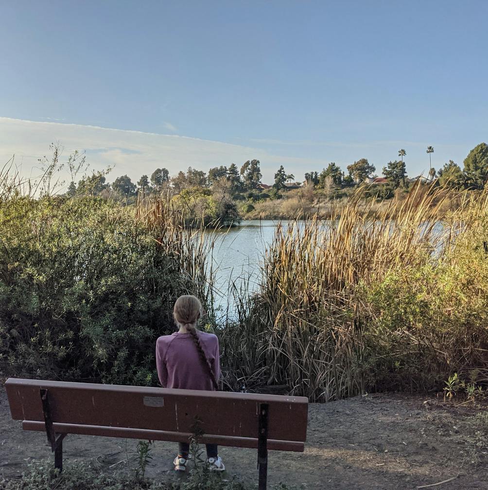 Woman sitting at a bench overlooking Guajome Lake in Guajome County Park San Diego 