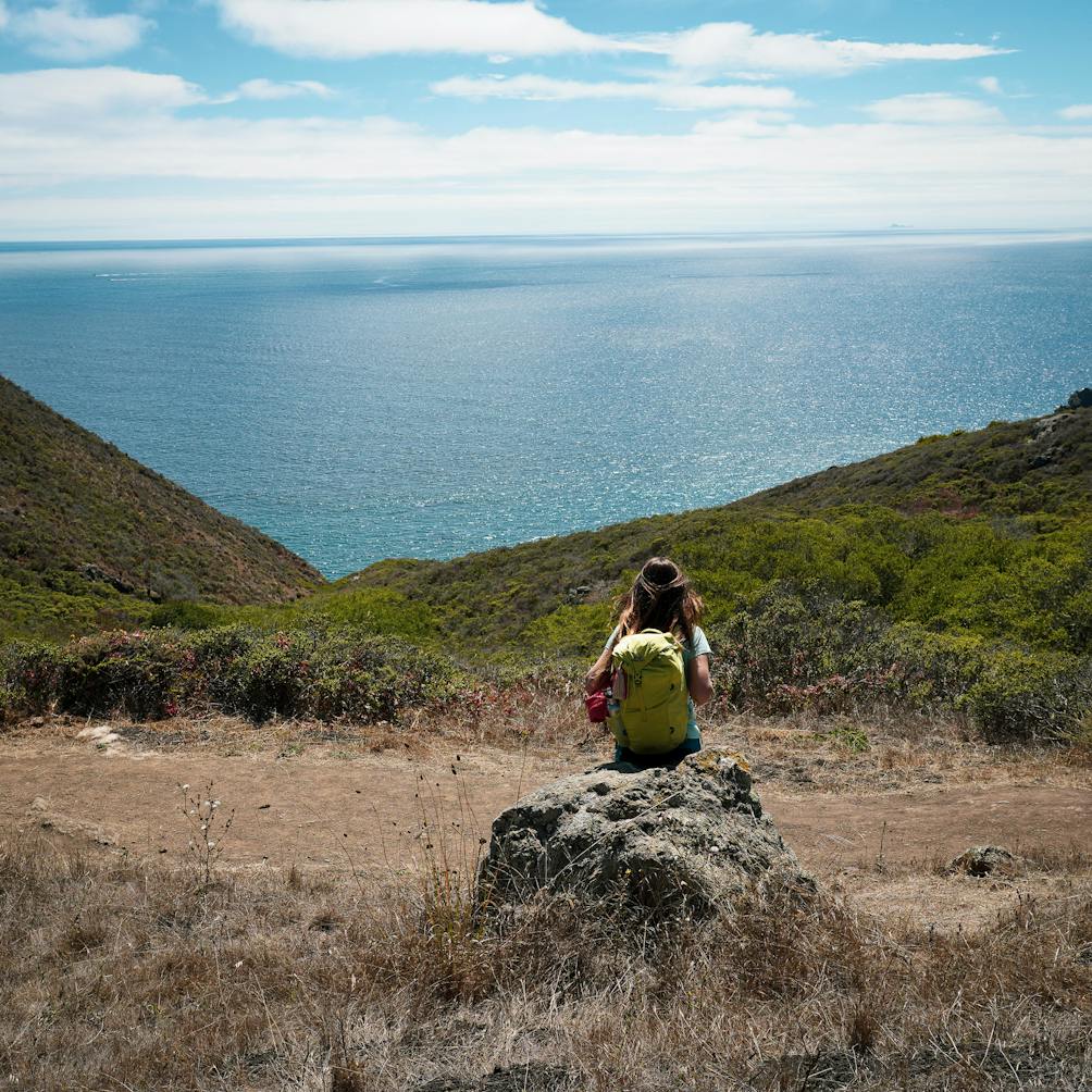 Woman resting on a rock overlooking the Pacific ocean on the Coastal Trail in the Marin Headlands 