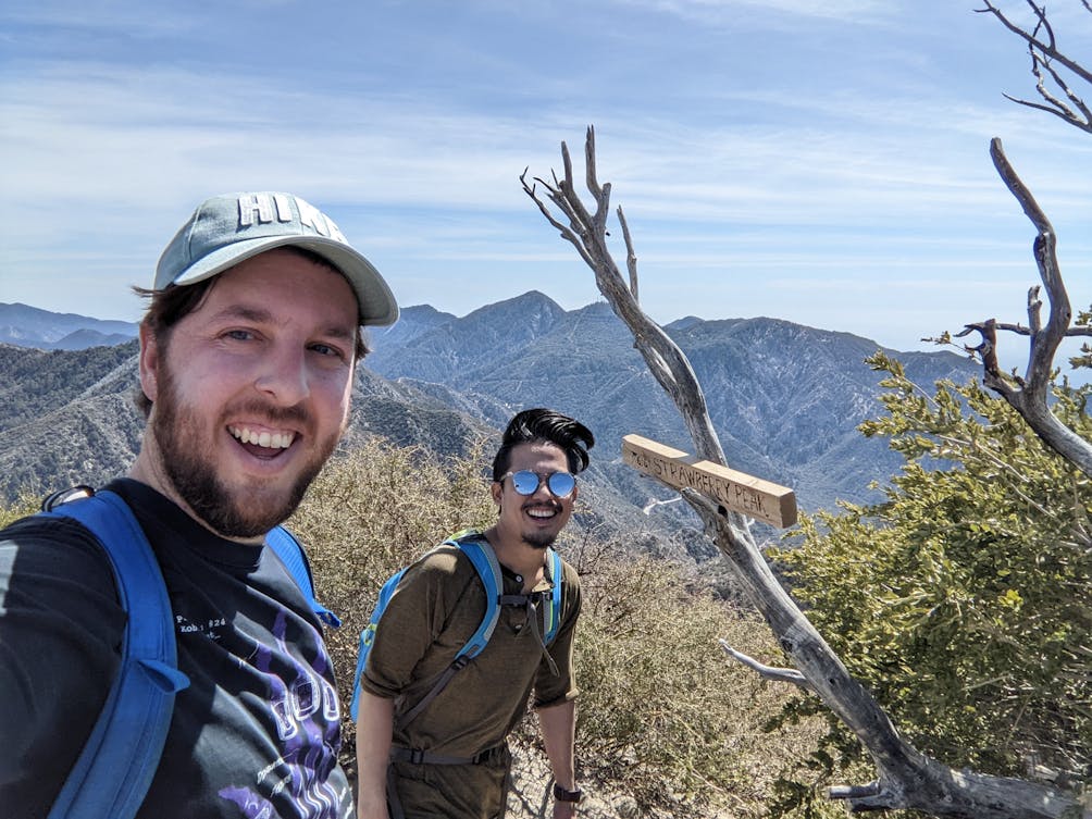 Two hikers taking a selfie on the trail in front of the Strawberry Peak sign in the San Gabriels 