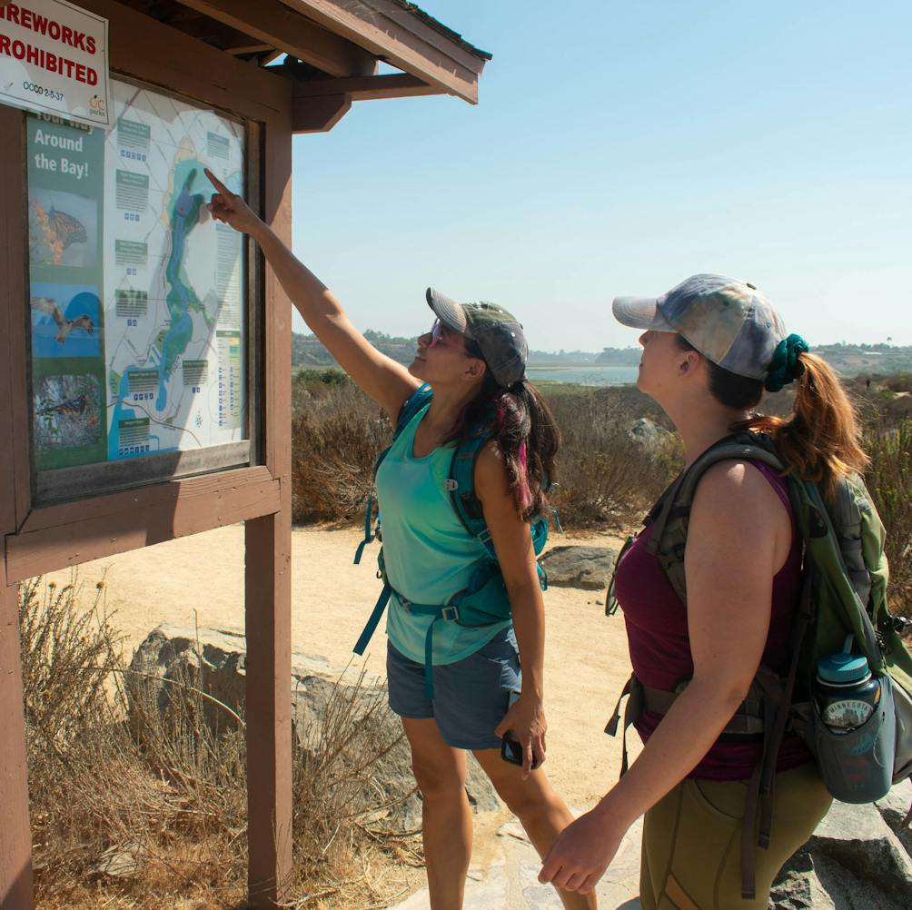 Two hikers at a trailhead map for Upper Newport Bay Nature Preserve in Orange County 