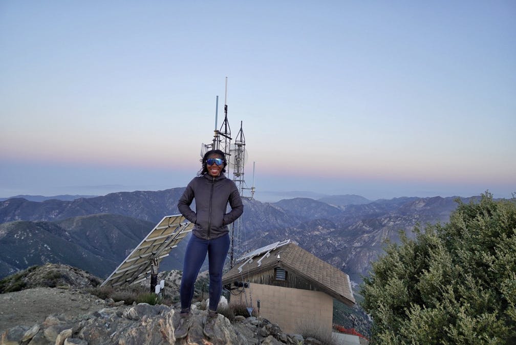 Woman standing in front of the old fire lookout at the summit of Josephine Peak in the San Gabriels