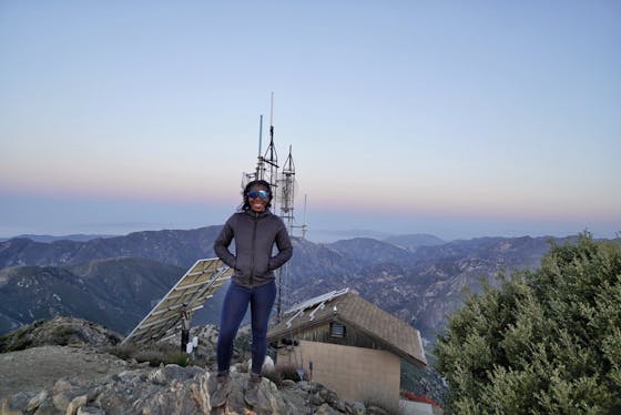 Woman standing in front of the old fire lookout at the summit of Josephine Peak in the San Gabriels