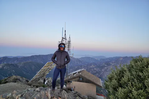 Woman standing in front of the old fire lookout at the summit of Josephine Peak in the San Gabriels