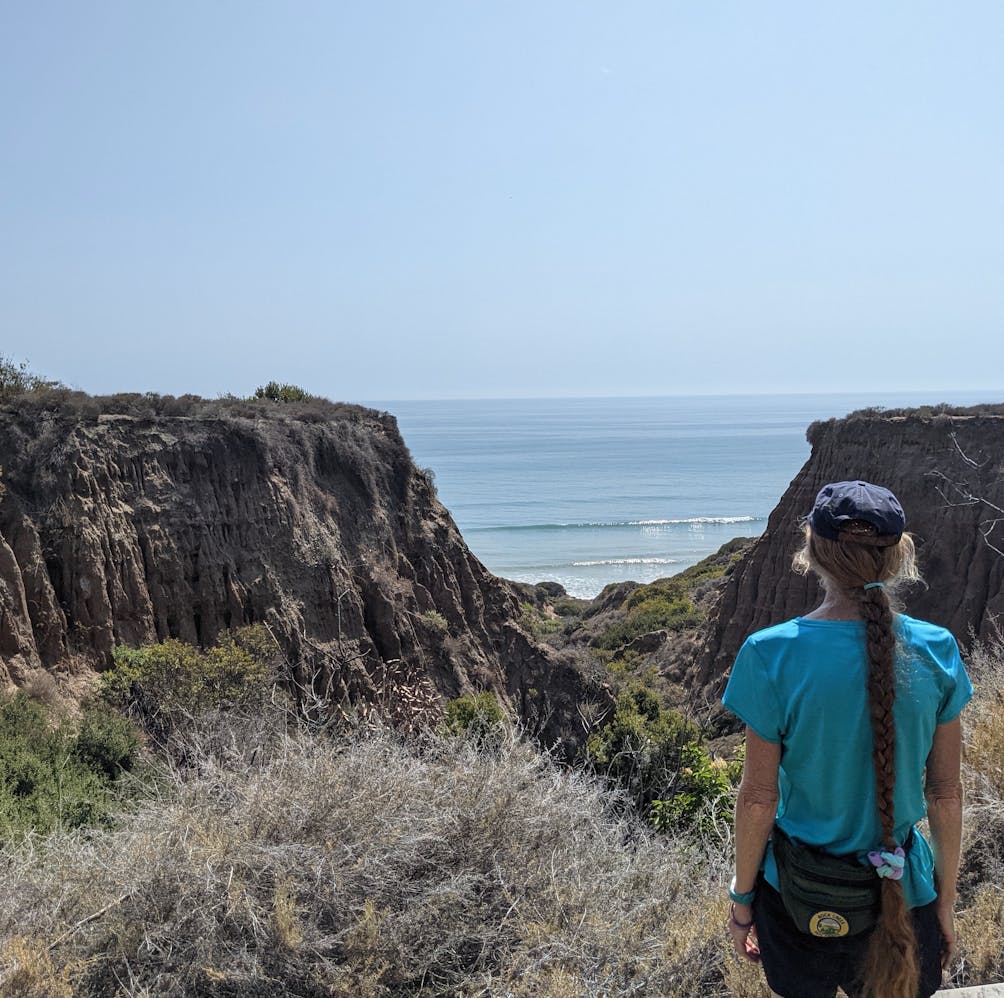 Woman standing on a bluff overlooking the sandstone rock canyon formation above San Onofre State Beach in San Diego County