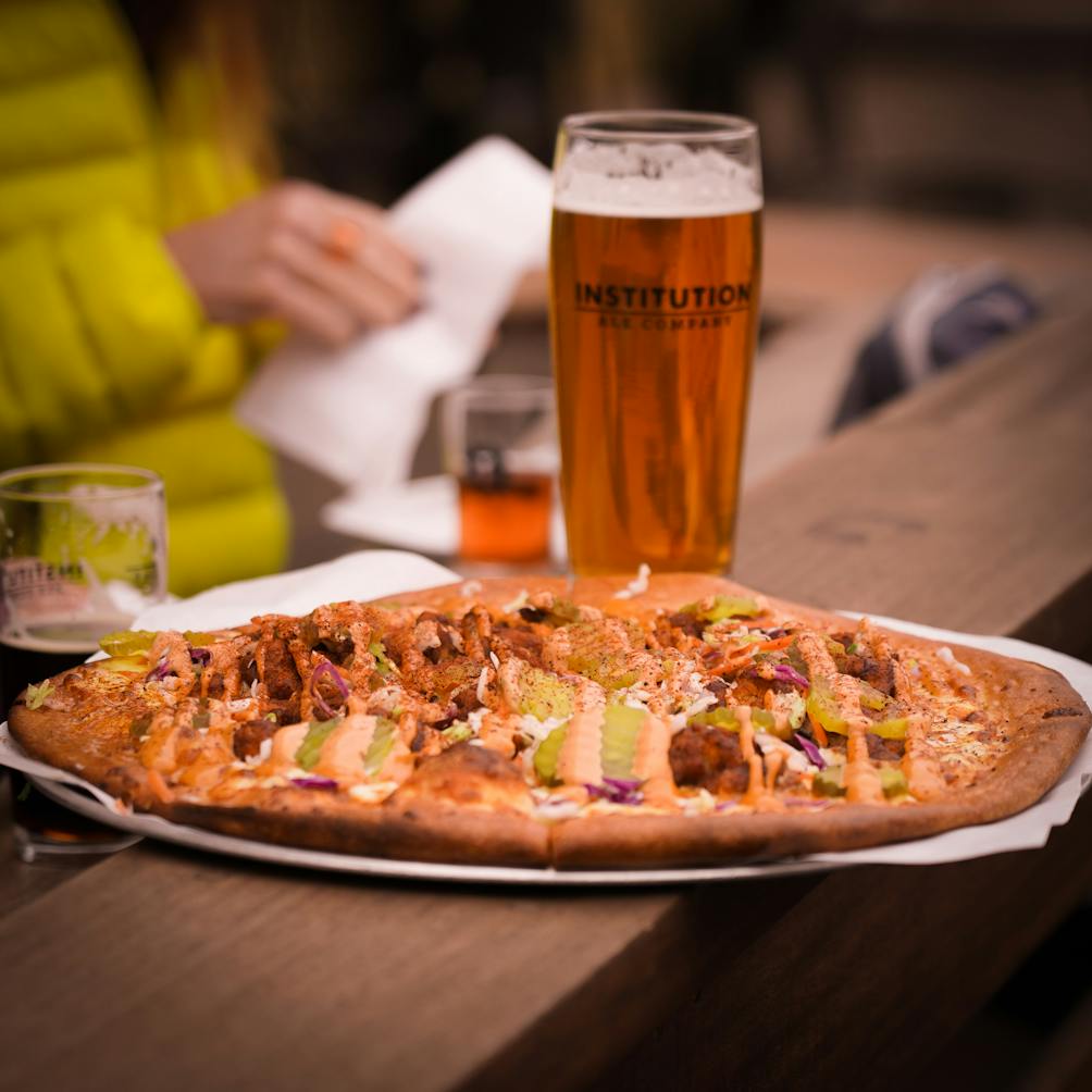 Institution Ale 12 oz beer next to a spicy fried chicken pizza 