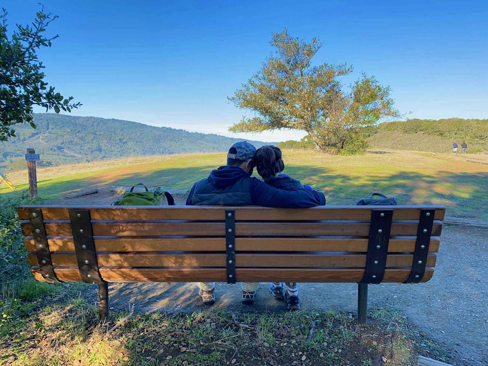 Two people cuddling on a bench overlooking an oak tree and hills at Edgewood Preserve in Woodside 